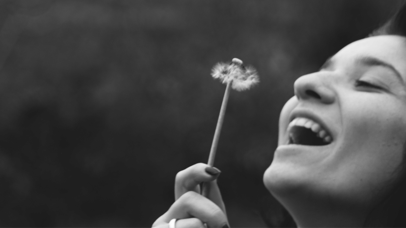 lachende Frau die eine Pusteblume anpustet