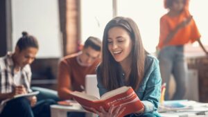 Gruppe von lernenden Leuten. Im Vordergrund eine Frau die ein Buch liest.