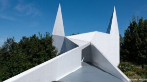 Siegerland_Autobahnkapelle - Die Architektur basiert auf dem Piktogramm für Autobahnkirchen. Das Gebäude besitzt einen quadratischen Grundriss und eine gefaltete, weiße Hülle mit zwei dreieckigen Türmen.