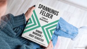 Jemand hält das Buch: Spannungsfelder Leben in Deutschland von Ahmad Mansour und Josef Schuster in der Hand (Cover Weiß mit grünen dreiecken)